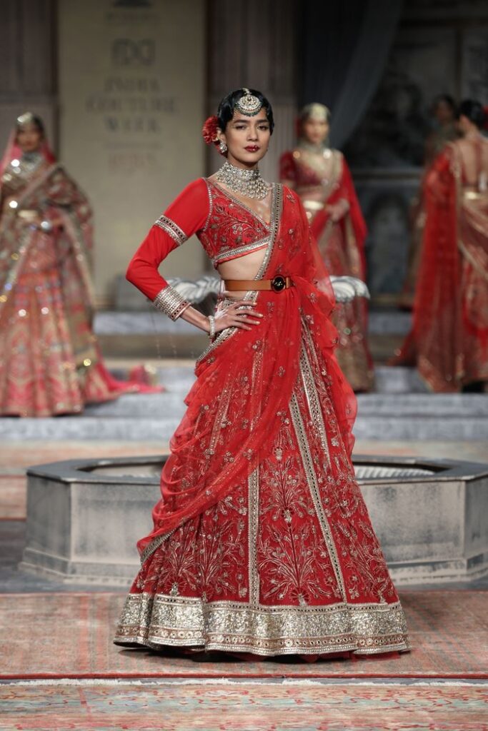 Model in exquisite red Indian bridal wear posing on a fashion show runway.