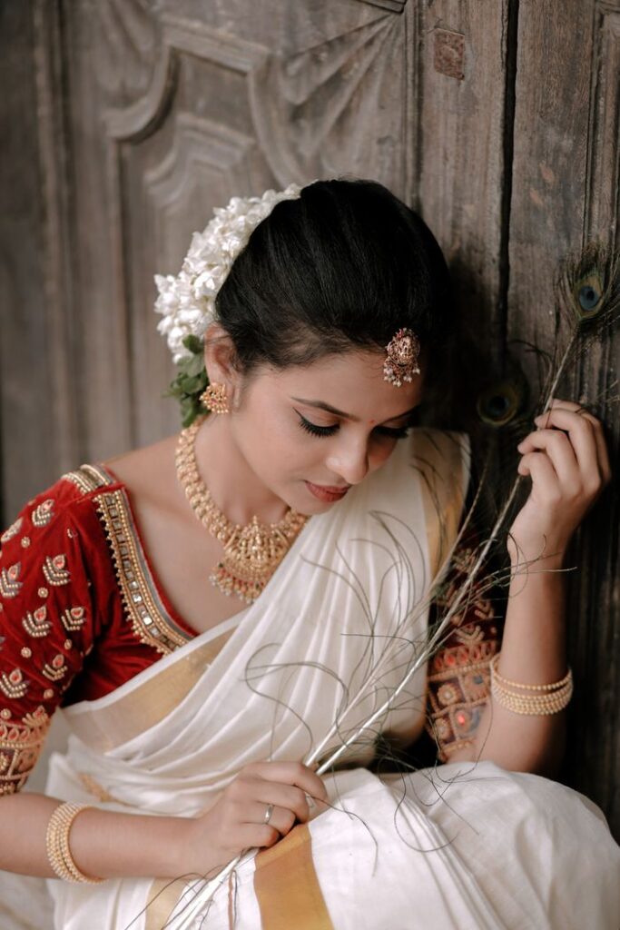 A woman in traditional Indian sari with jewelry, seated against a wooden backdrop, exuding elegance.
