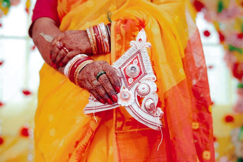 Captivating image of a Bengali bride's hands adorned with mehendi, jewelry, and traditional saree.