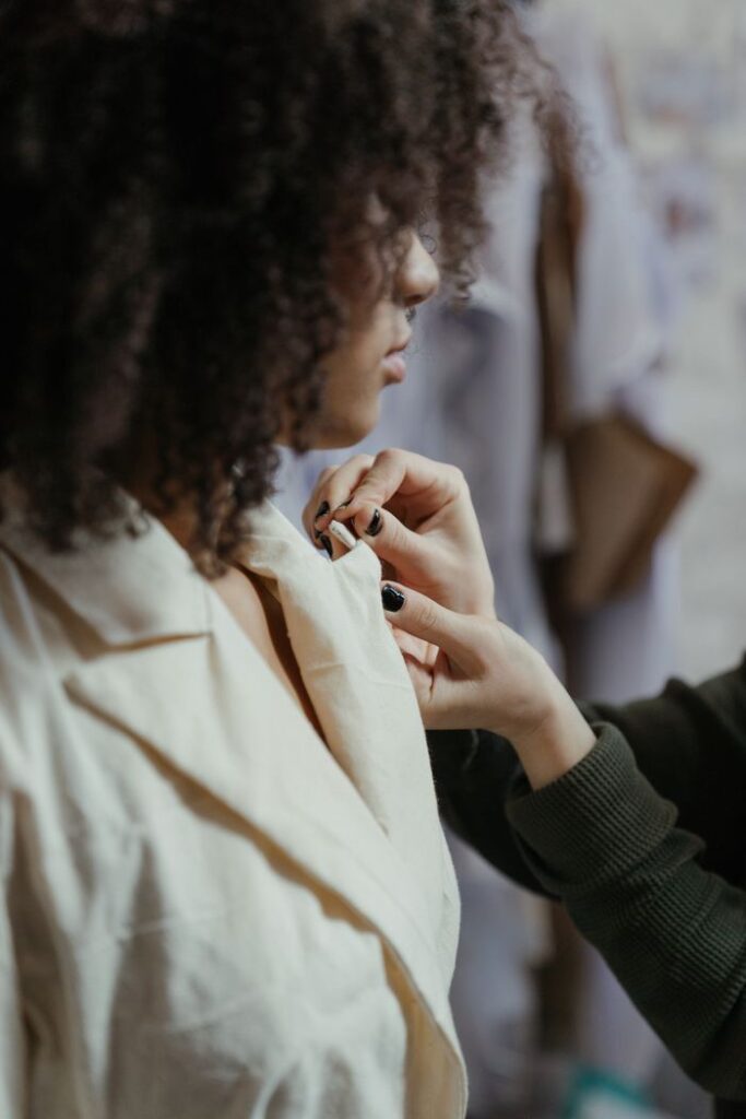 Close-up of a tailor adjusting the collar of a model's outfit in a fashion studio.
