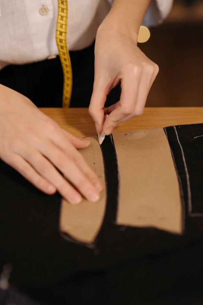Close-up of a tailor's hands tracing a sewing pattern on black fabric with precision and skill.
