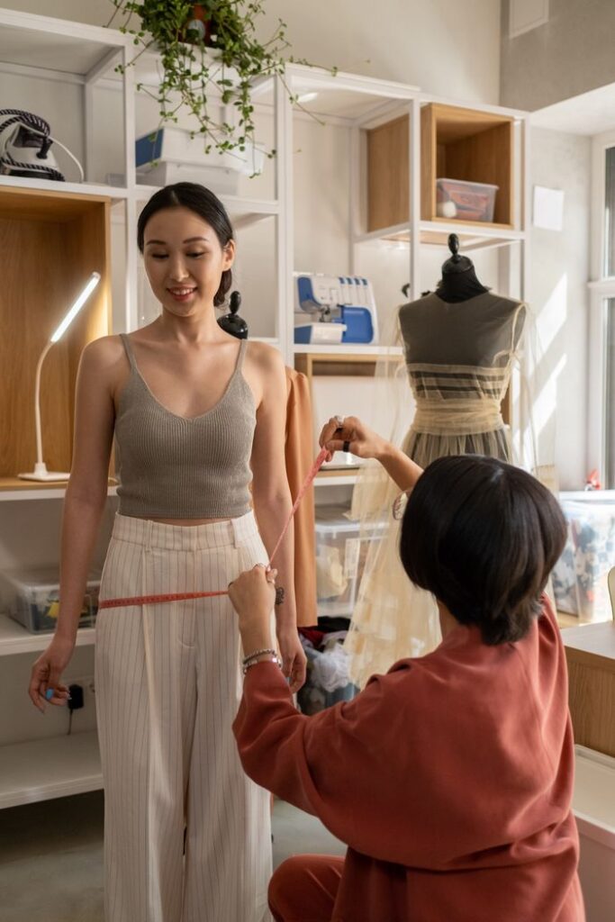 A fashion designer measuring a model's waist in a stylish studio setting.